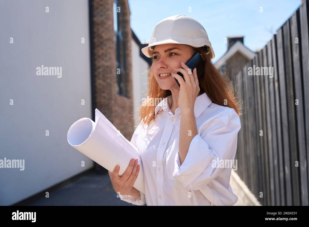 Woman cadastral service worker talking phone holding papers and blueprints Stock Photo