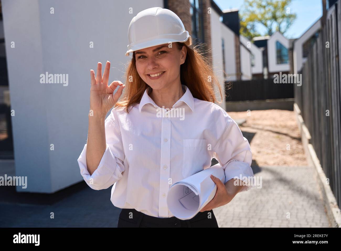 Woman architect with blueprints in hands and hardhat showing ok sign Stock Photo