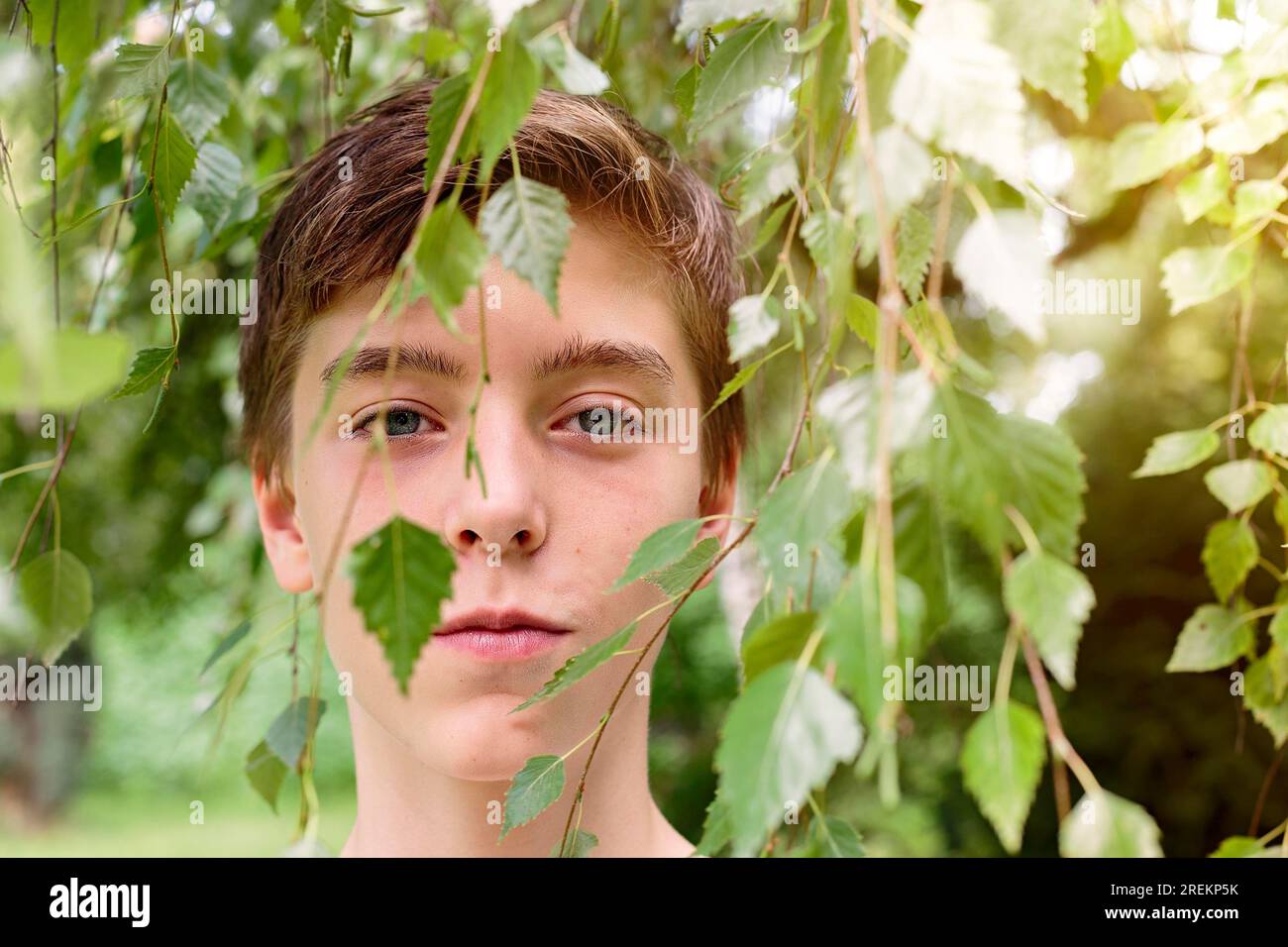 Portrait of a teenage boy hidden by some leaves Stock Photo