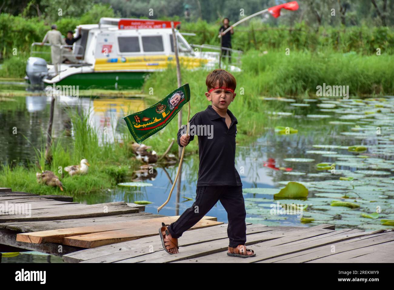 Srinagar, India. 28th July, 2023. A Shiite young Muslim boy holds an Islamic flag as he walks on the wooden foot-bridge during a Muharram procession in Srinagar. Muharram is a month of mourning in remembrance of the martyrdom of Imam Hussain, the grandson of Prophet Muhammad (PBUH). (Photo by Saqib Majeed/SOPA Images/Sipa USA) Credit: Sipa USA/Alamy Live News Stock Photo