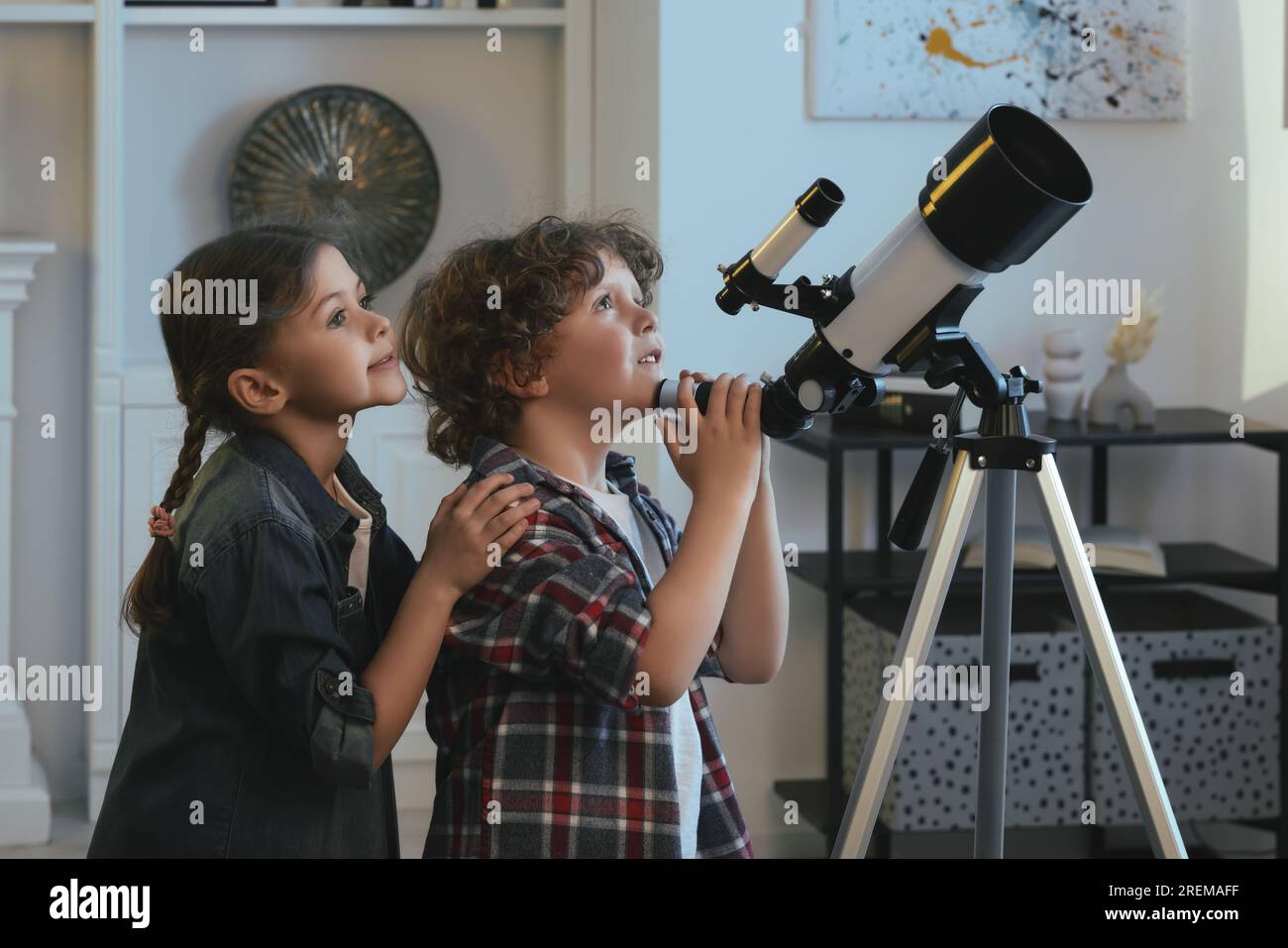 Cute little children using telescope to look at stars in room Stock
