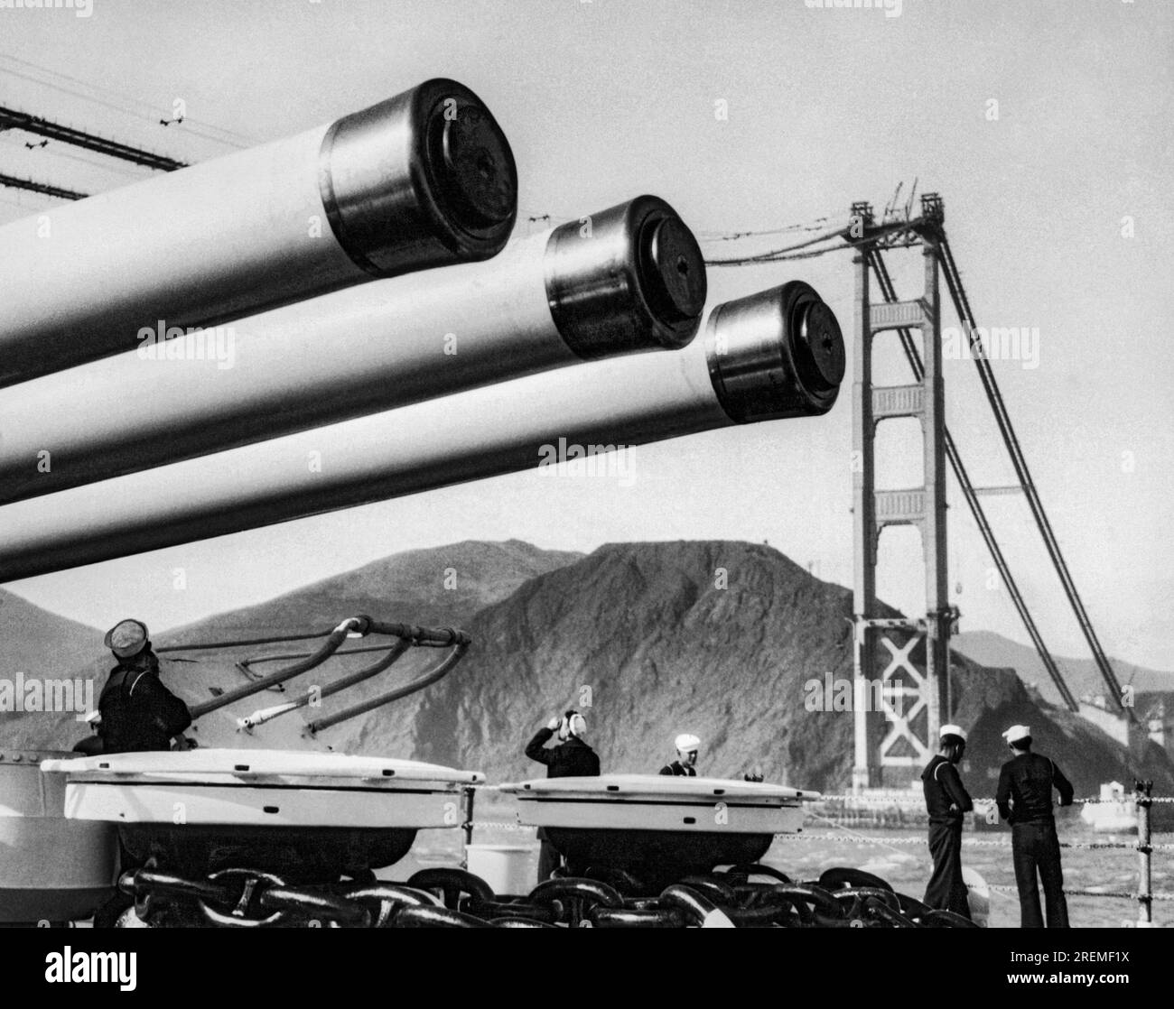 San Francisco, California:   c. 1936 A U. S. Navy battleship cruises under the cables of  the Golden Gate Bridge as it is being built Stock Photo