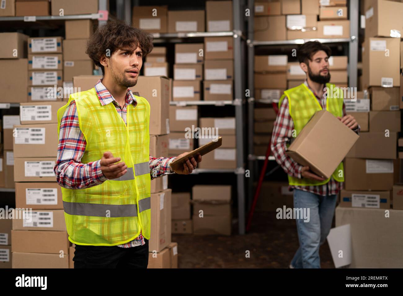Team of two warehouse workers shipping order detail on digital tablet check goods on shelves with goods inventory in factory warehouse. Logistic Stock Photo
