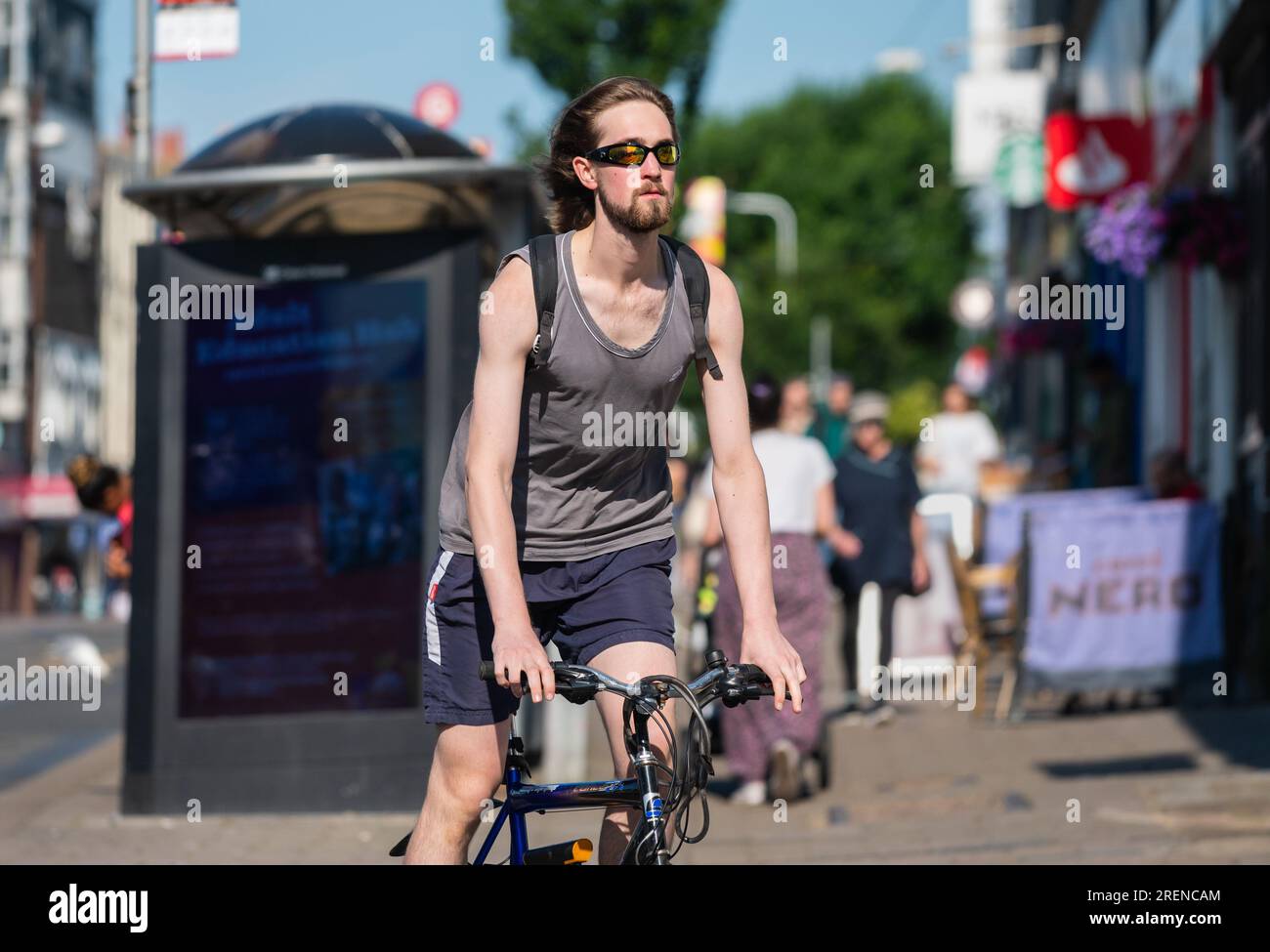 Young male cyclist, young man riding bicycle on a road in a busy urban city in Summer, without wearing a helmet, in England, UK. Healthy lifestyle. Stock Photo