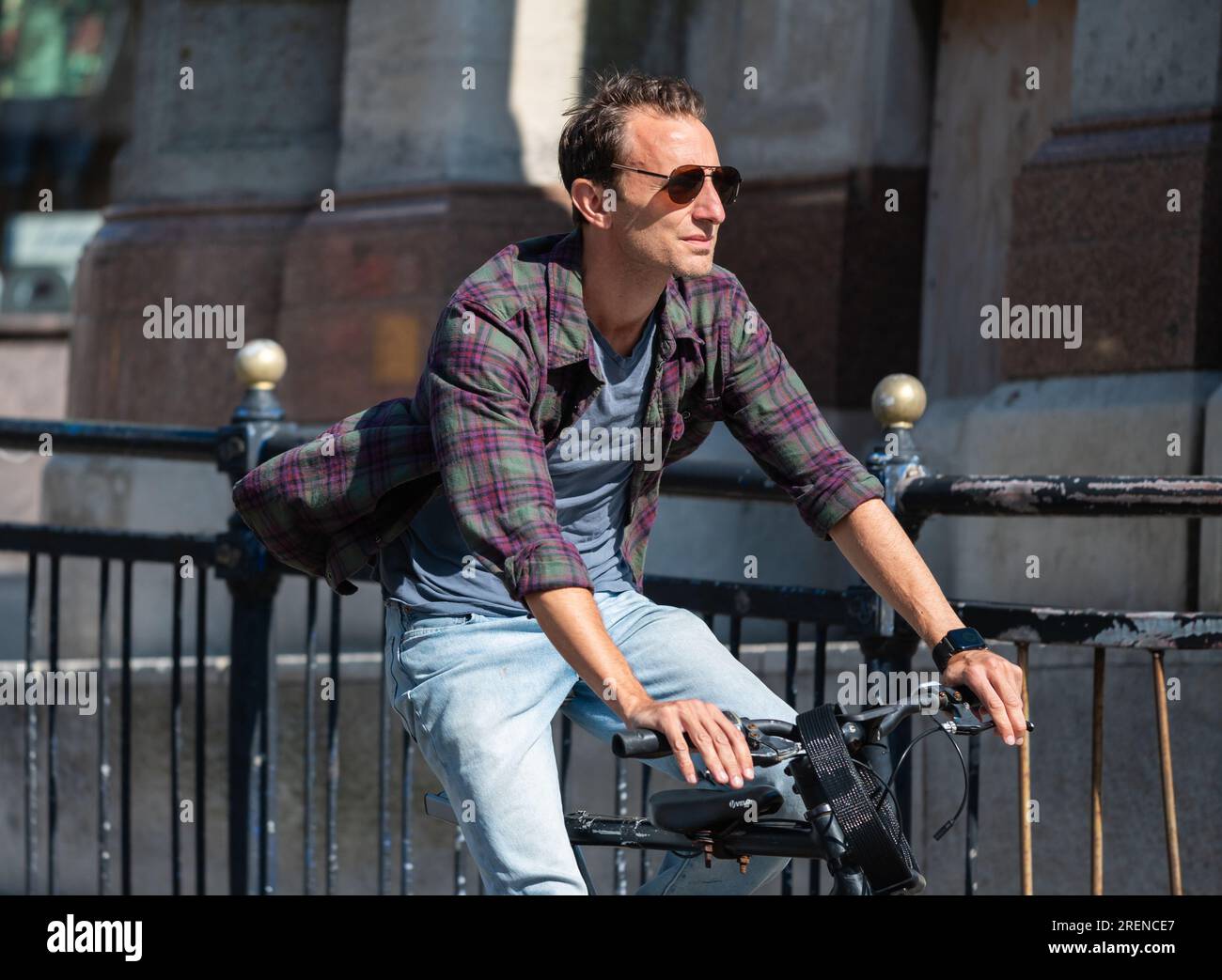 Young male cyclist, young man riding bicycle on a road in a busy urban city in Summer, without wearing a helmet, in England, UK. Healthy lifestyle. Stock Photo