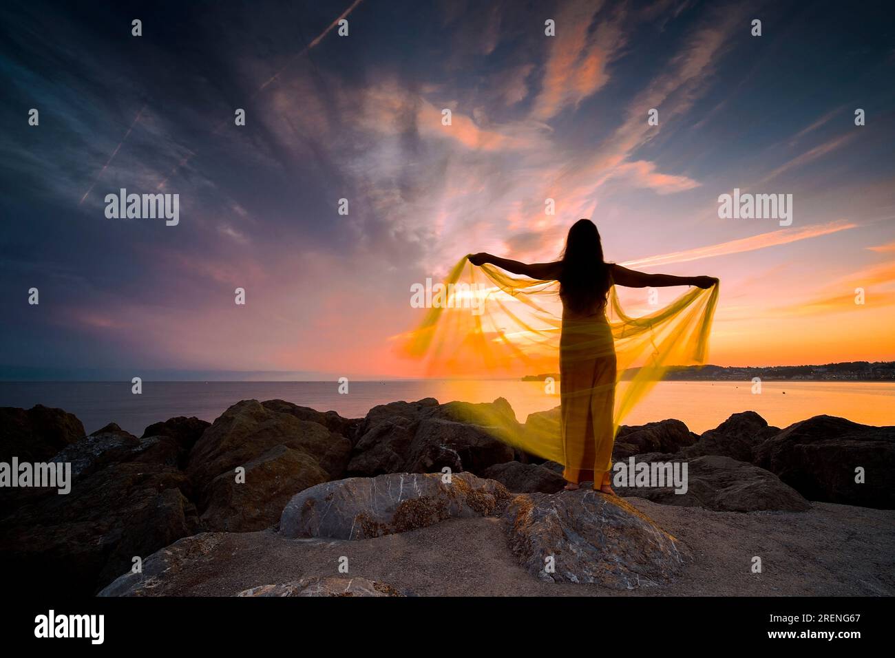 woman in a yellow dress and cape observing a magnificent sunrise on the French Basque coast IV Stock Photo