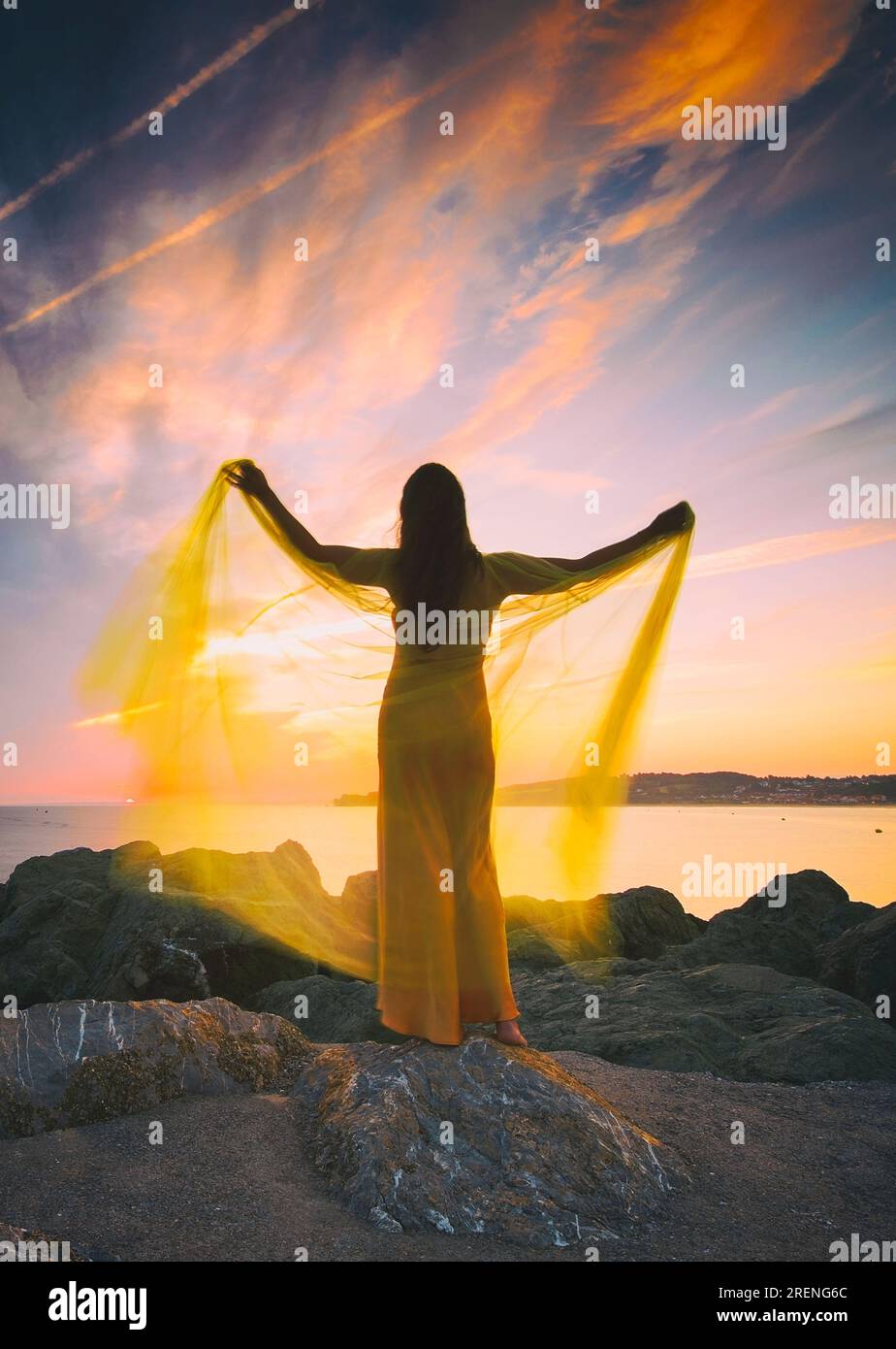 woman in a yellow dress and cape observing a magnificent sunrise on the French Basque coast VI Stock Photo