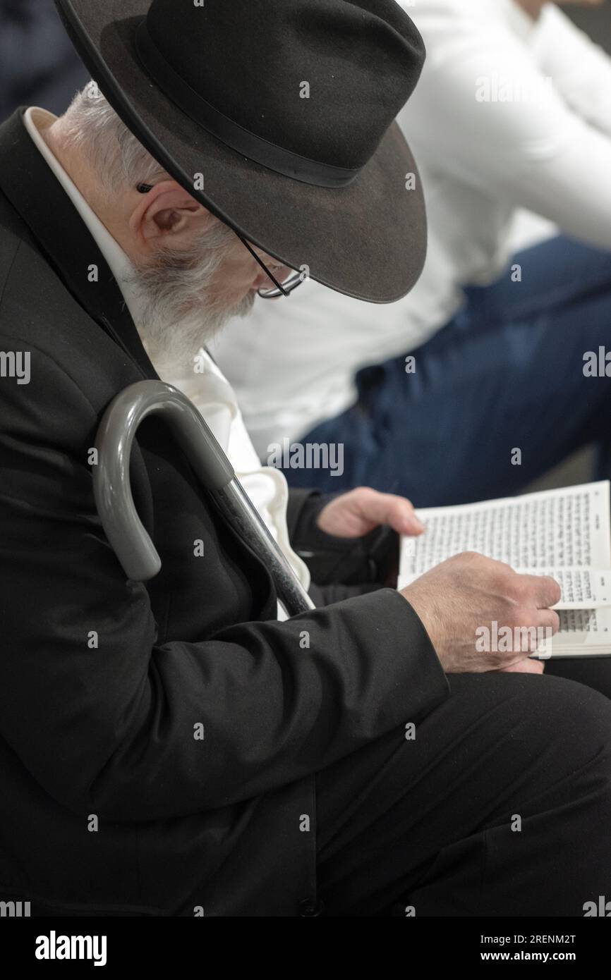 An older orthodox Jewish man with a cane & hearing aid, recites morning prayers on Tisha B'av