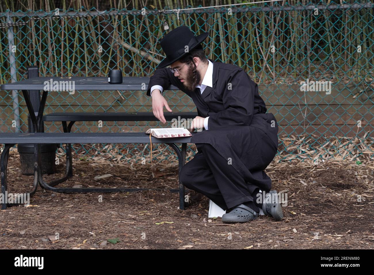 At Tish B'Av morning services, an orthodox Jewish man prays outdoors alone on a low seat commensurate with the mourning laws for the day. In New York. Stock Photo