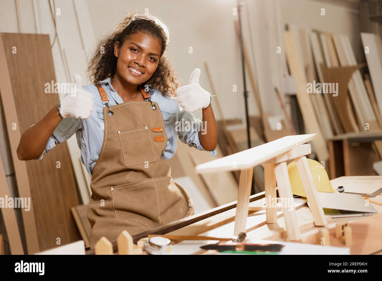 Happy carpenter woman african black smiling in wood workshop enjoy making handmade wooden furniture business. Stock Photo