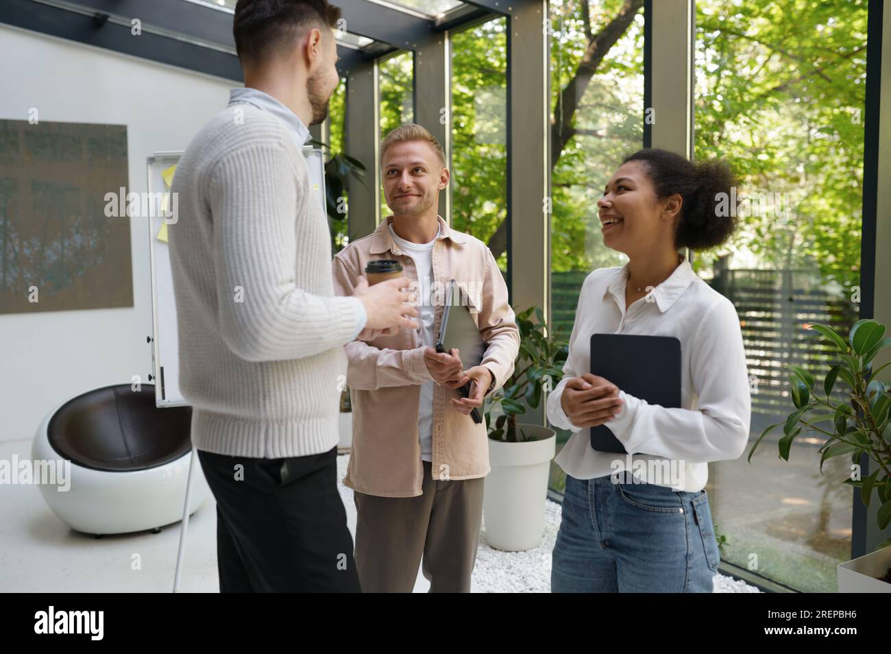 Smiling cheerful colleagues group standing at workplace and chatting Stock Photo