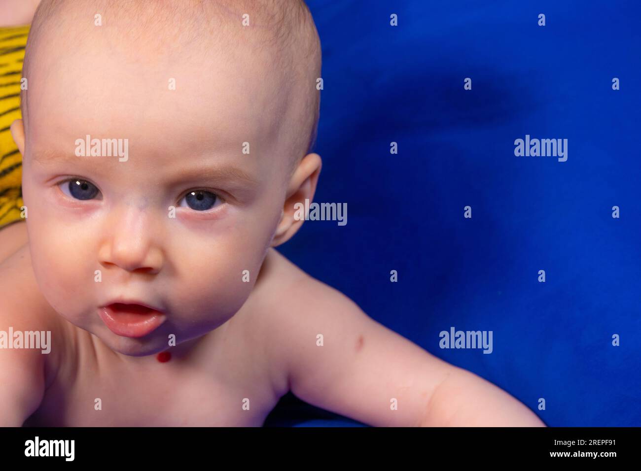a baby on a blue background with a wooden rattle Stock Photo