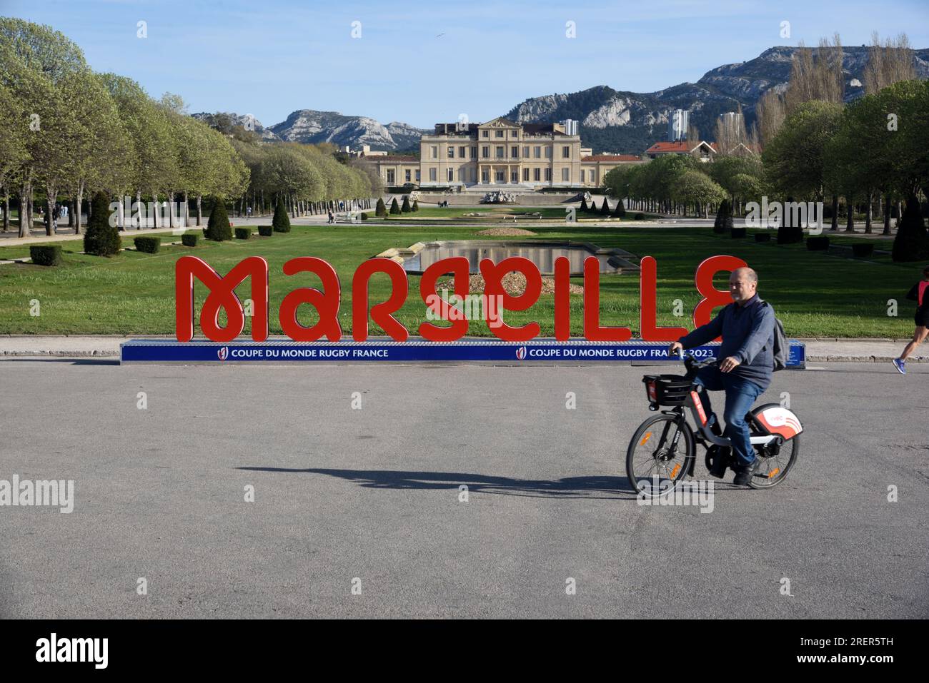 Cyclist Cycling Past Giant Red Letters of Sign Marseille in front of Chateau Borely, Park and Garden Marseille France Stock Photo