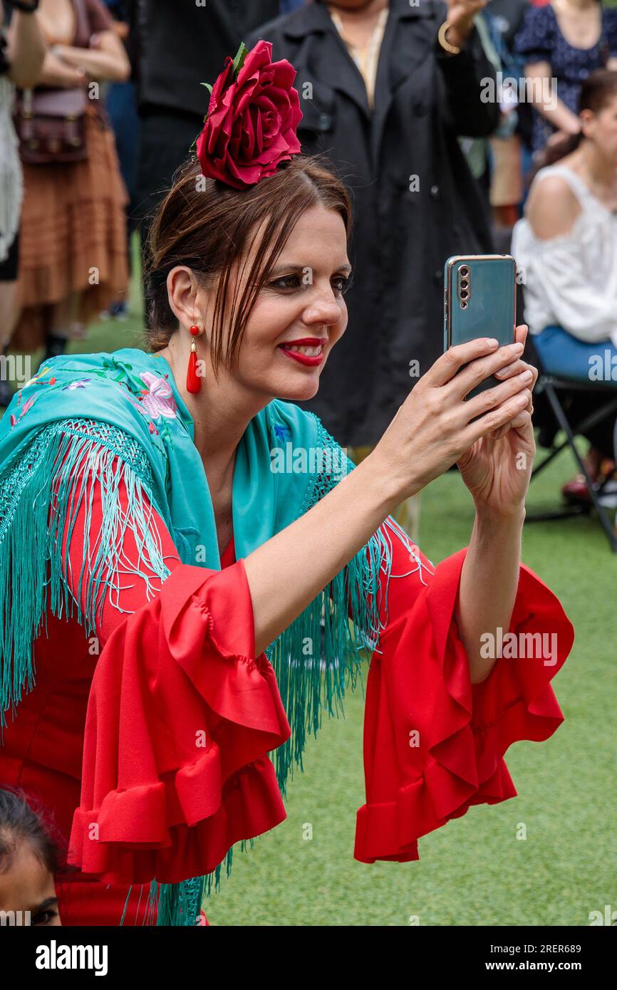 Feria de Londres, Wembley Park, UK. 29th July 2023. Feria De Londres, the UK's largest celebration of Spanish culture, holds it's free 2 day festival in Wembley Park for the first time. A lady in traditional Spanish dress films the festivities on her mobile phone. Photo by Amanda Rose/Alamy Live News Stock Photo
