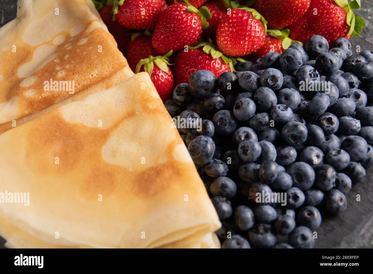 photo lots of fresh juicy berries lying next to pancakes on a plate top view Stock Photo