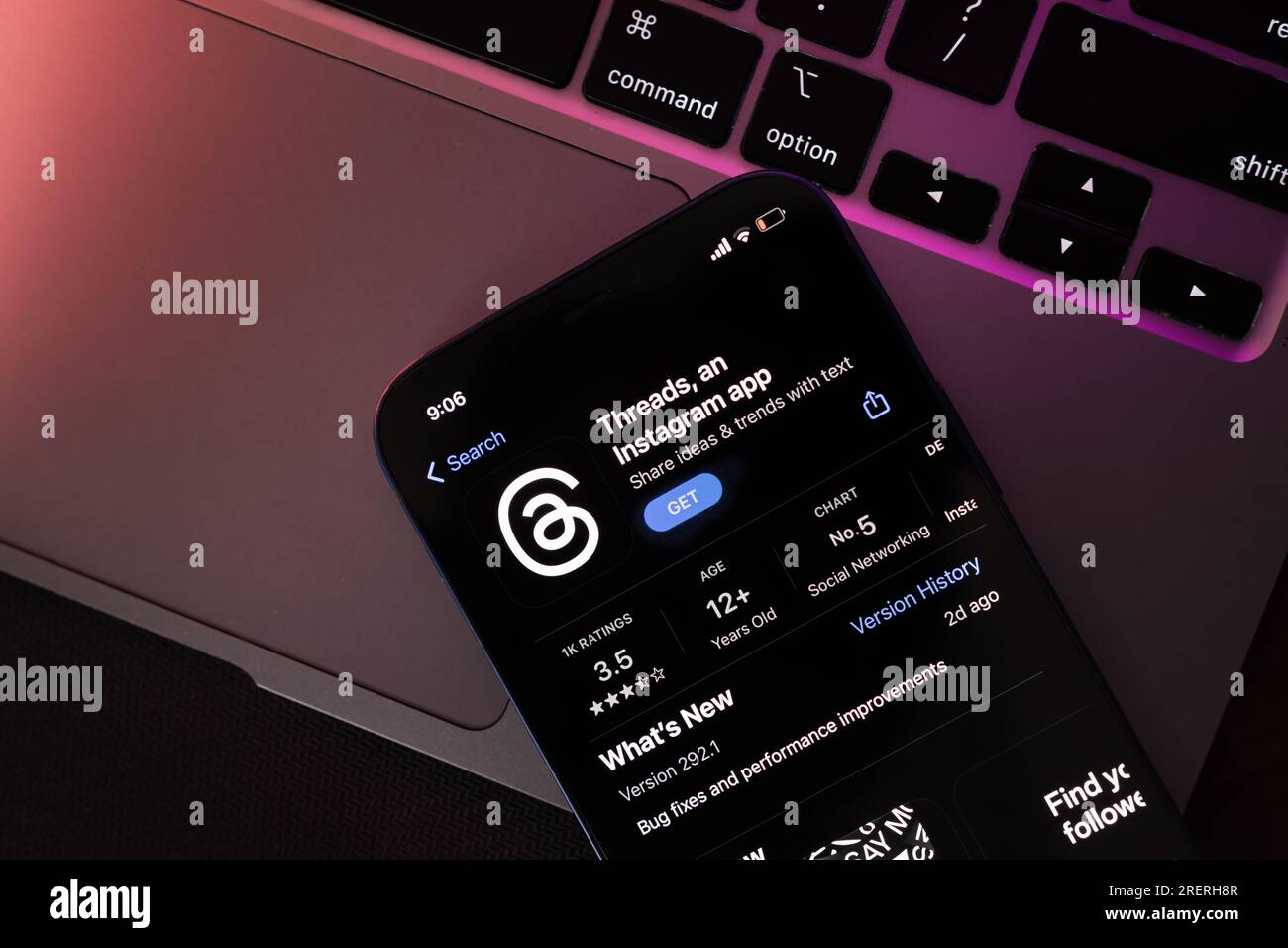 Threads App opened in App Store on a phone with a laptop in the background Stock Photo