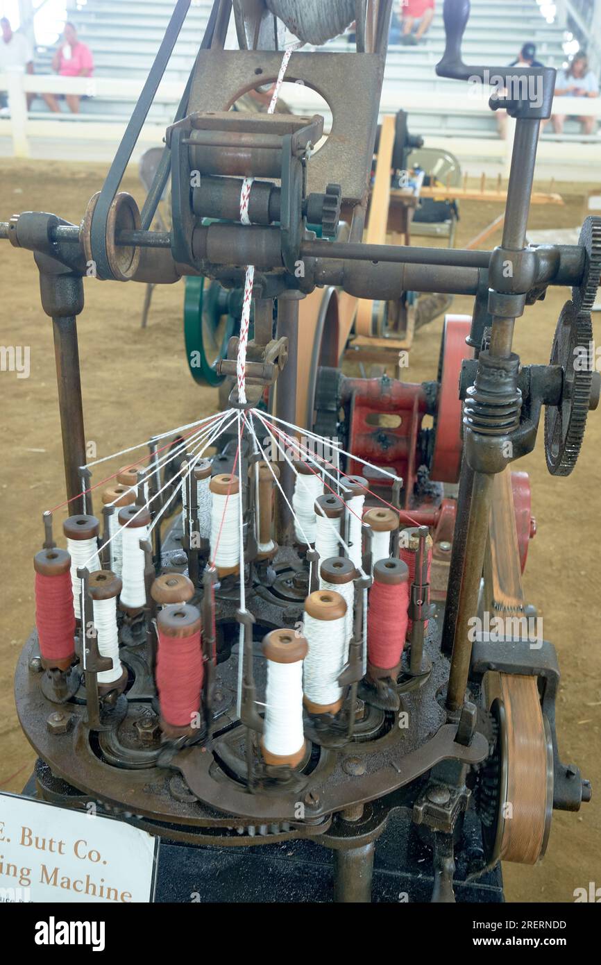 An antique braiding machine creates rope from multiple spindles of threads.  The machine is belt driven and powered by a small gasoline engine. Stock Photo