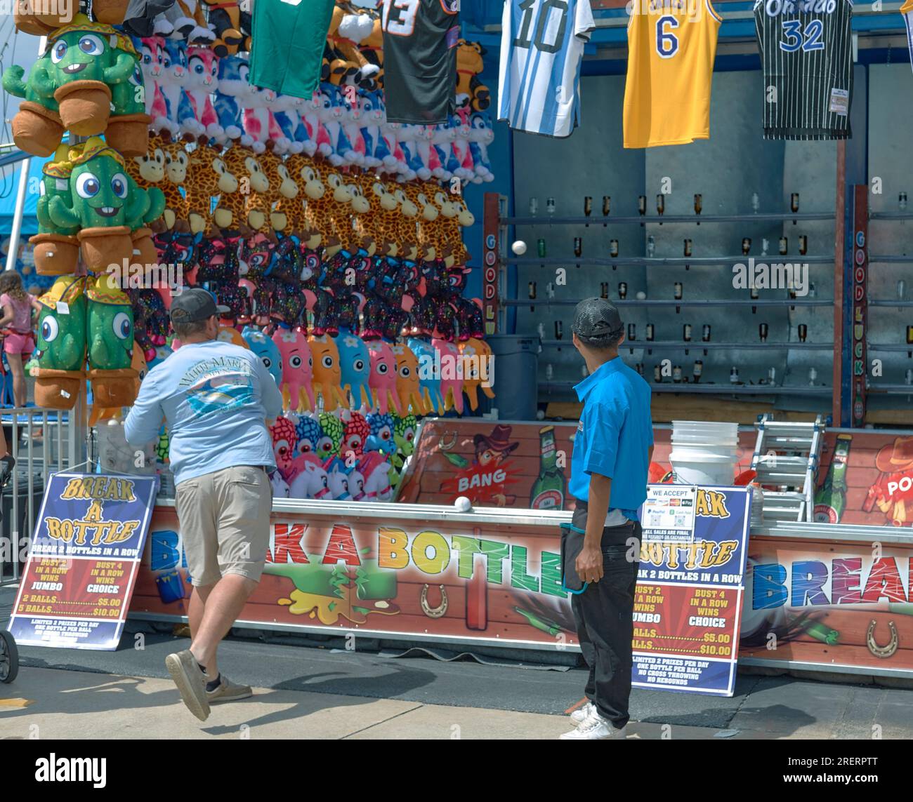 A man attempts to throw baseballs at bottles to win prizes on the midway at the 2023 Delaware State Fair, Harrington, Delaware USA. Stock Photo
