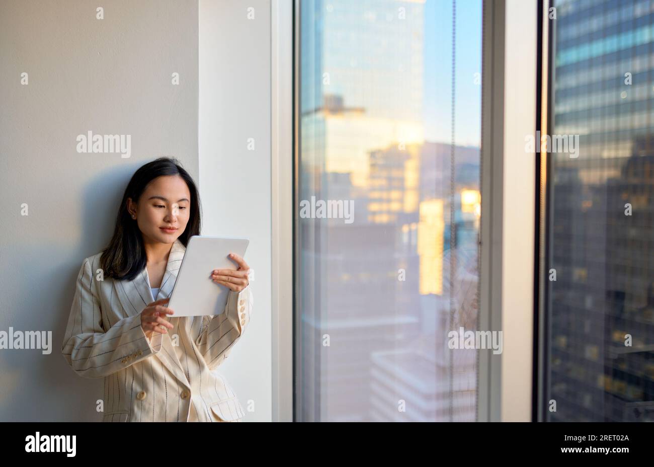 Young Asian business woman using digital tablet standing in office at window. Stock Photo
