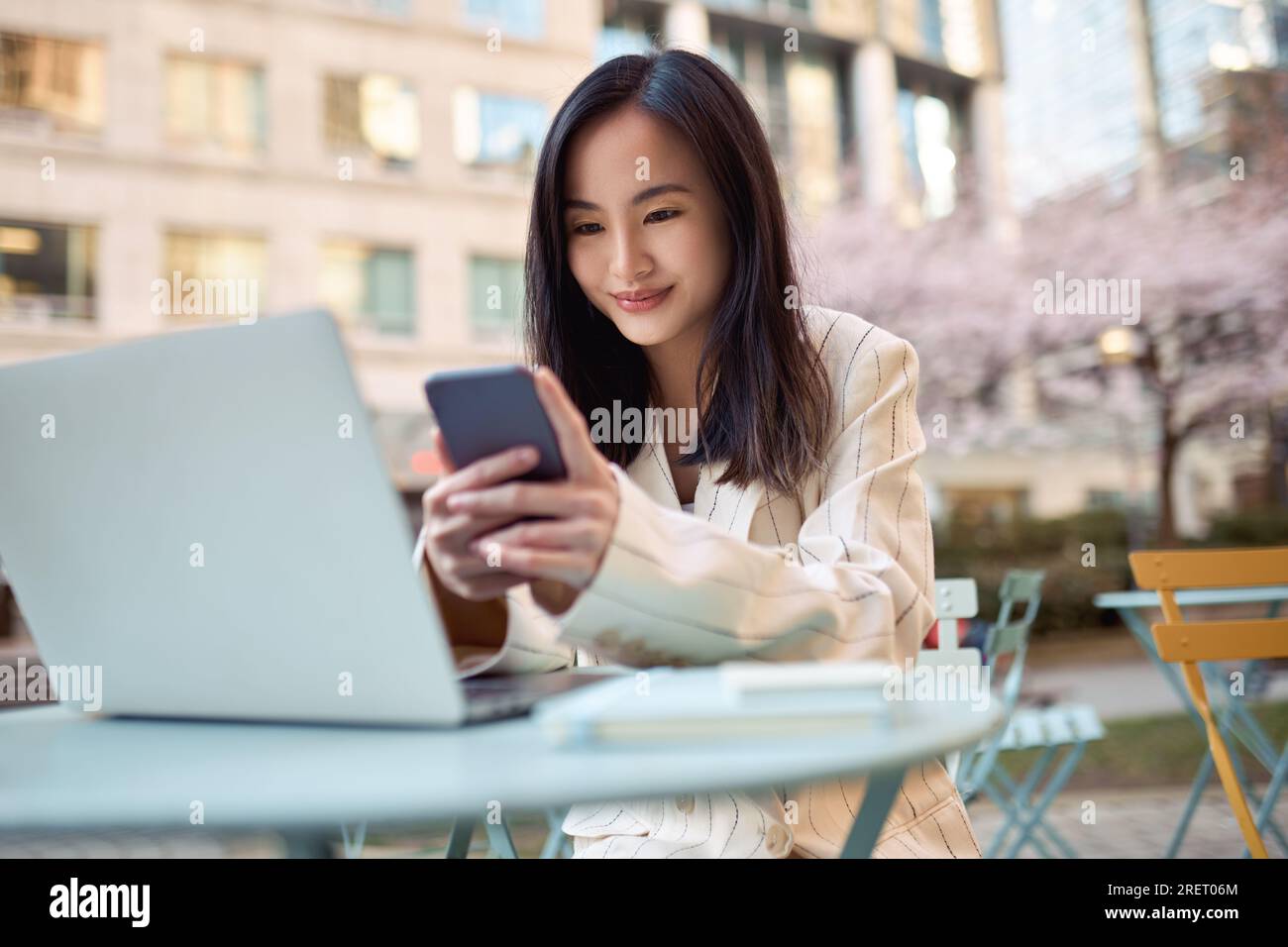 Young cute smiling Asian woman student using mobile phone and laptop ...