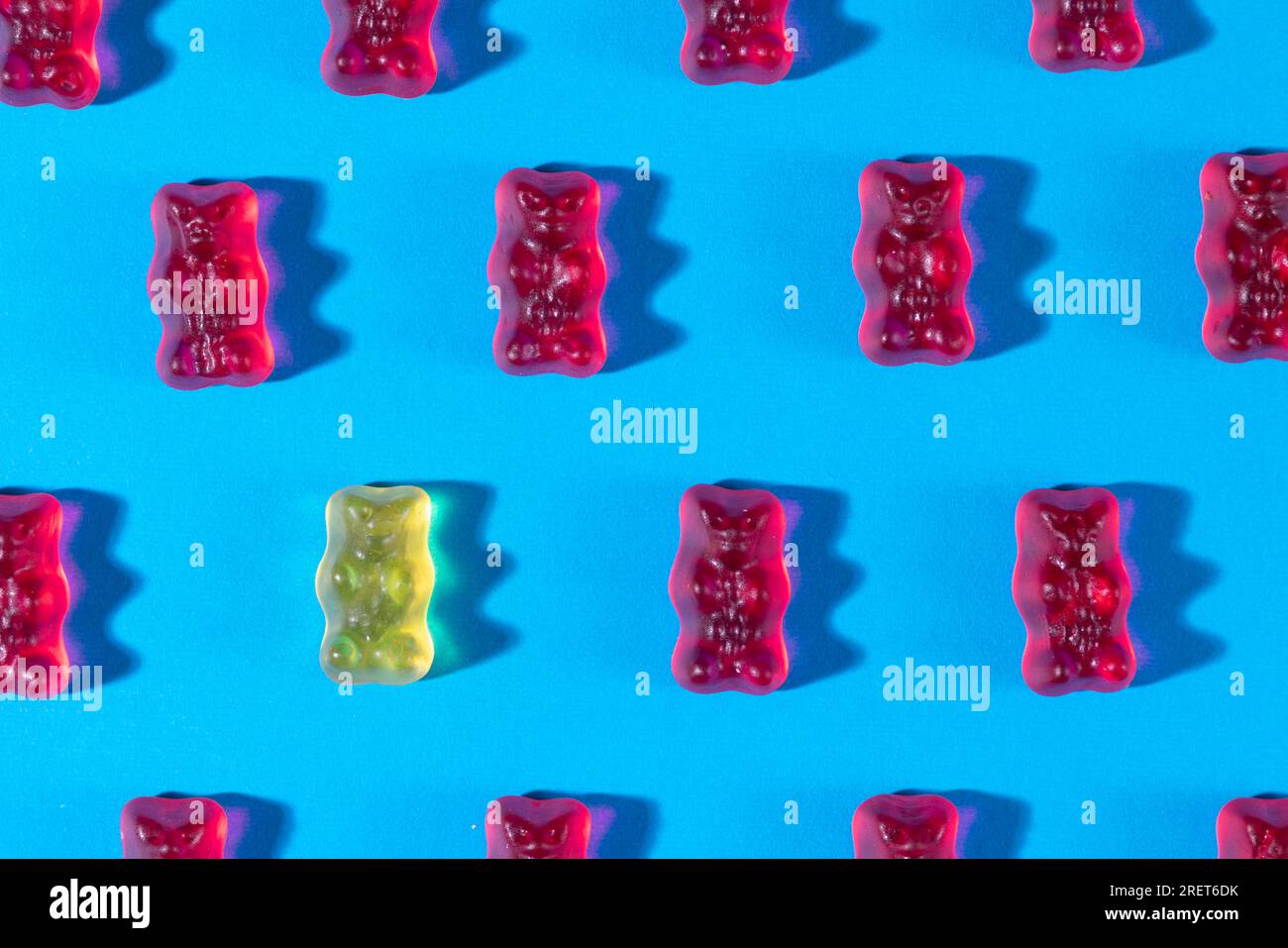 Red gummy bears and a yellow one in rows, on a blue background Stock Photo