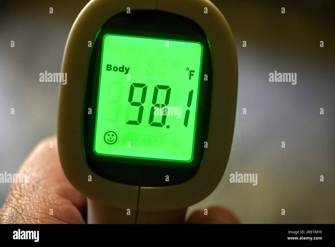 Hand holding a temporal thermometer with green digital reading in