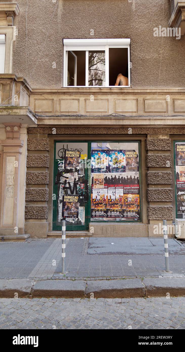 Grey building with promotional posters as a tattooed man stands in the window. Sofia, Bulgaria. July 29, 2023 Stock Photo