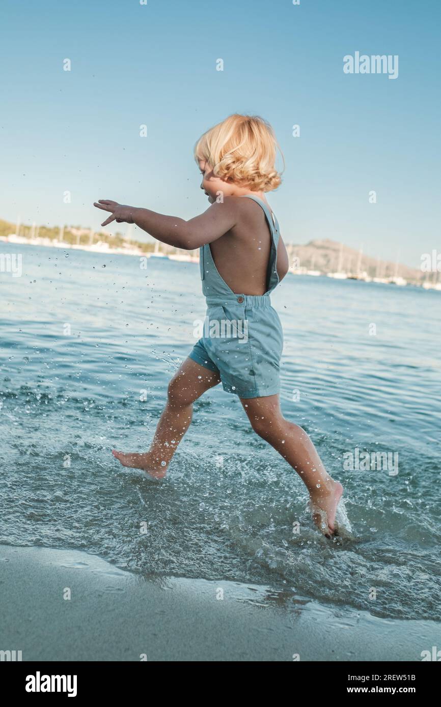 Side view of full body anonymous barefoot child enjoying and playing in rippling sea under bright blue sky Stock Photo