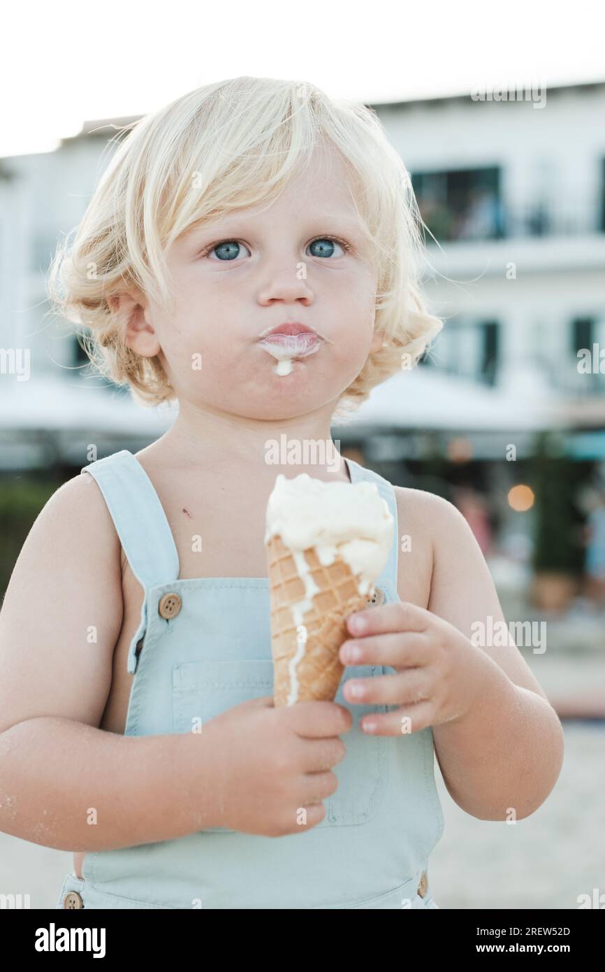 Fair haired child eating ice cream cone while standing on blurred