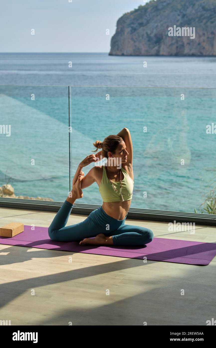 Side view of fit barefoot female sitting in Mermaid pose on mat while practicing yoga on sunny day on terrace Stock Photo Alamy