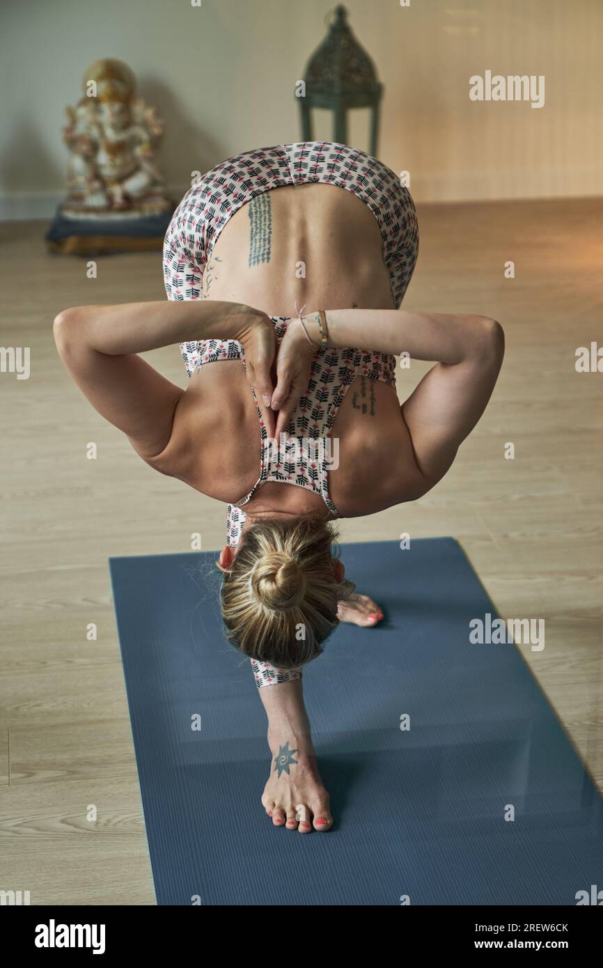 Back view full body of anonymous barefoot woman in activewear doing Parshvottanasana while practicing yoga on mat in light studio Stock Photo