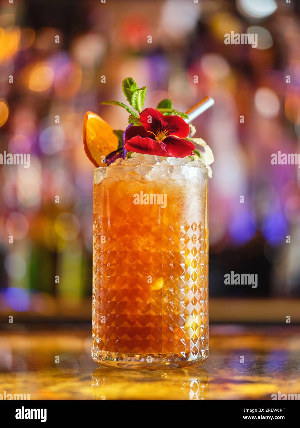 Glass of long drink cocktail with ice cubes and decorations served on counter in modern bar on blurred background with bokeh Stock Photo