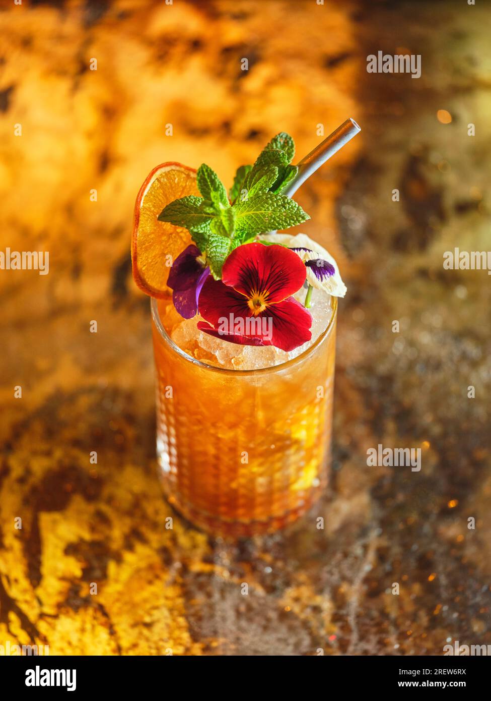 From above of glass with alcoholic long drink cocktail decorated with edible flower and dried orange served on counter of bar Stock Photo