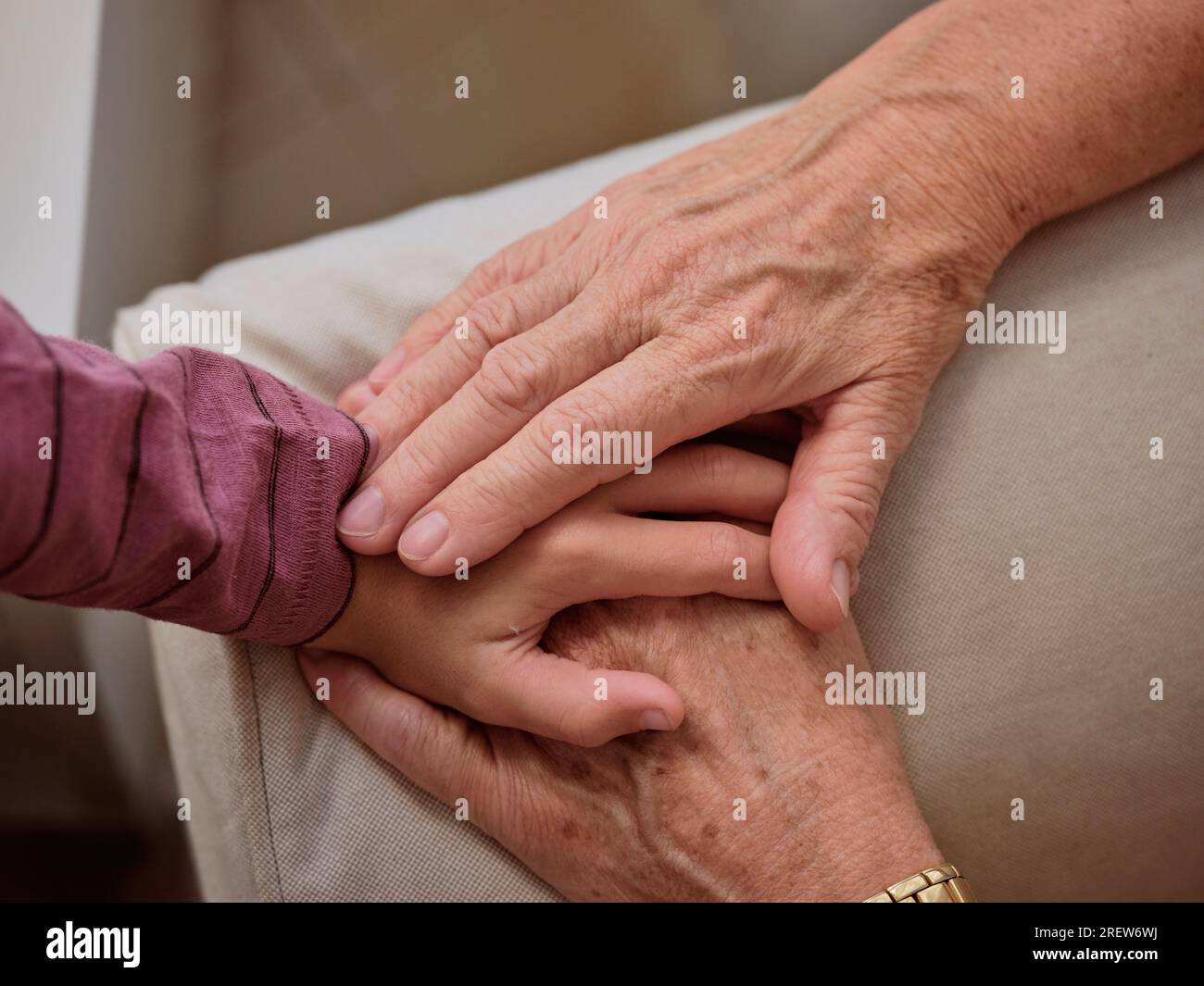 Crop anonymous grandparent touching hand of faceless grandchild on armrest while sitting on comfortable couch in living room at home Stock Photo