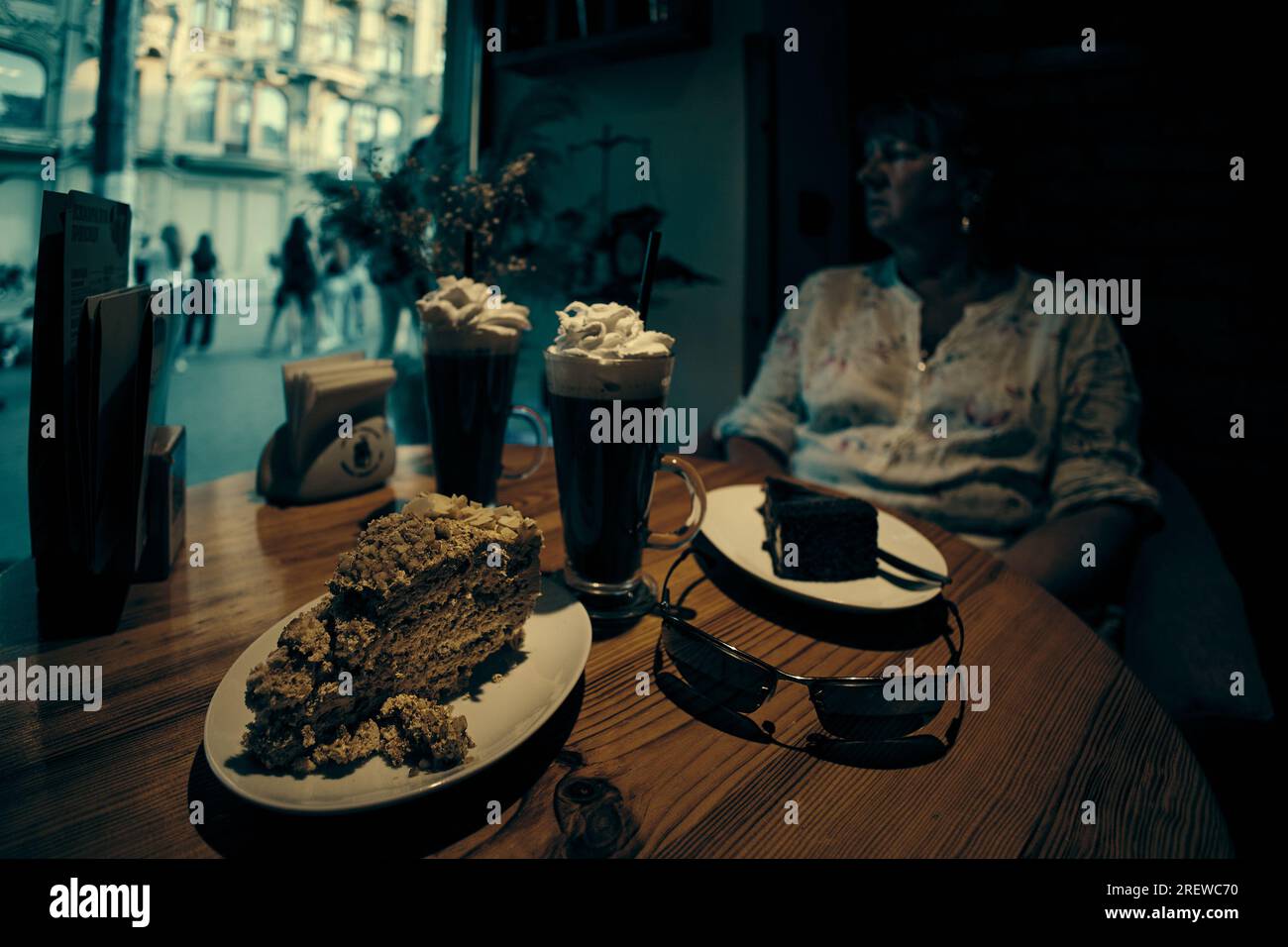 Two cakes and Irish coffee on the table and a pretty woman looks thoughtfully out the window in the background Stock Photo