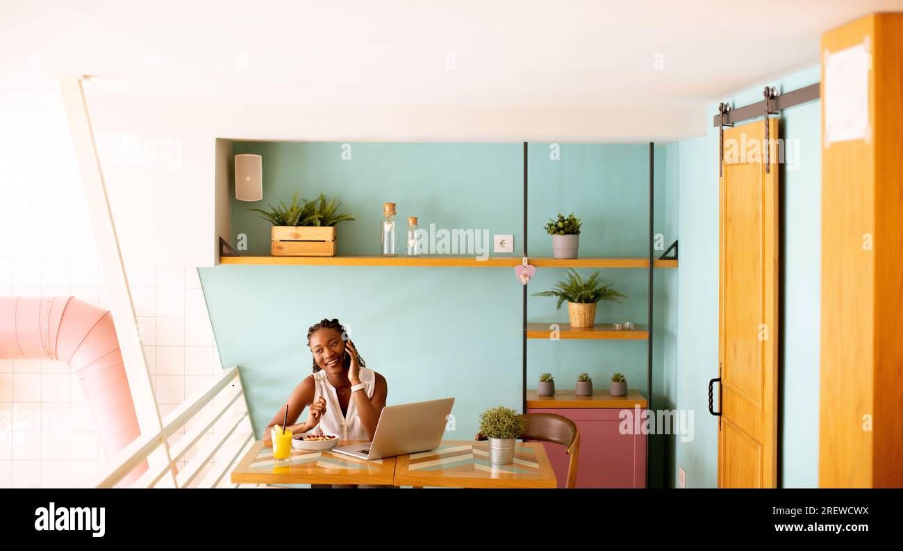 Pretty young black woman drinking coffee while working on laptop in the ...
