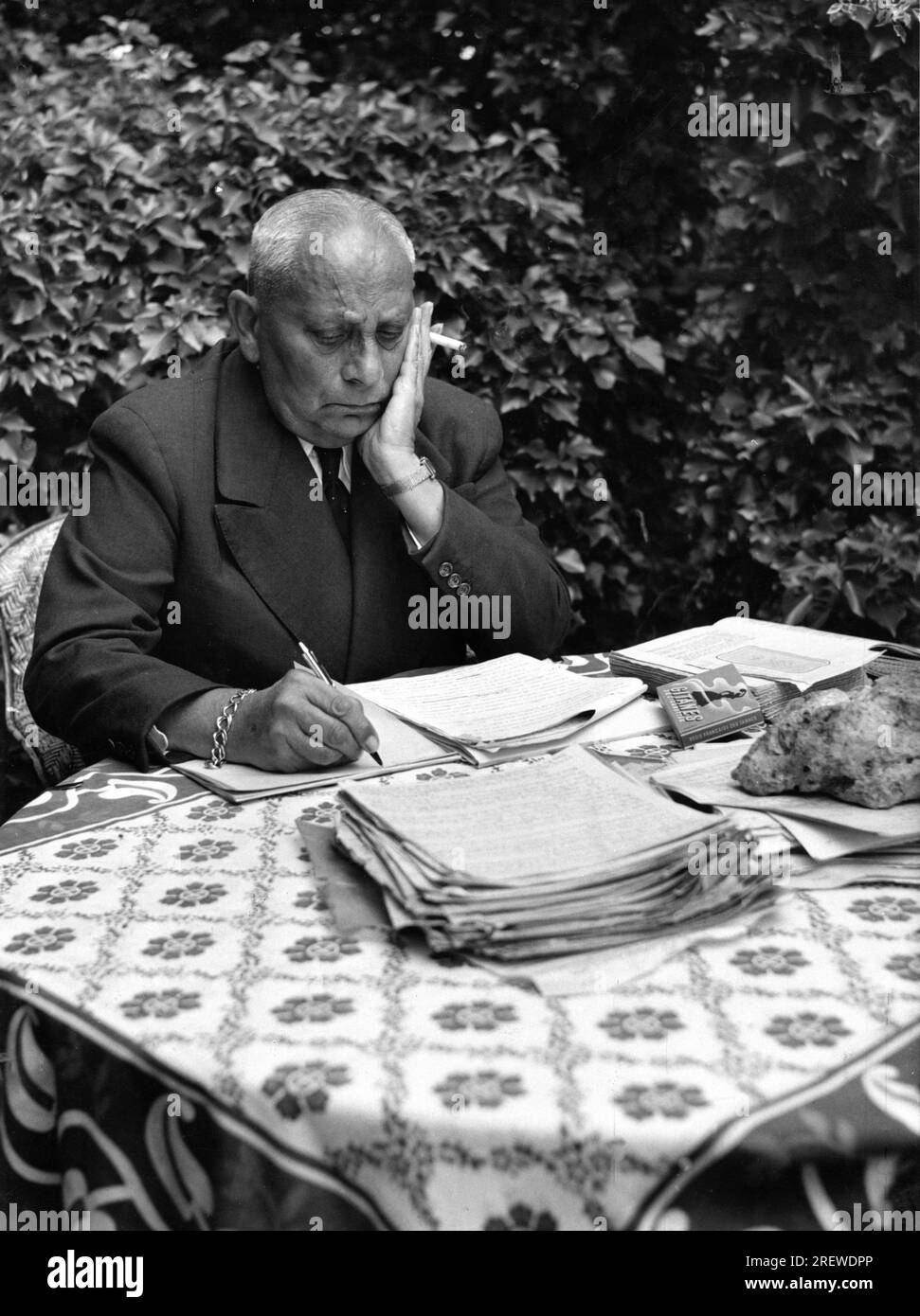 ERICH von STROHEIM at his home Maurepas in France on the outskirts of a hamlet close to Paris  in 1954 writing his novel DANS L'OMBRE D'UNE CATHEDRALE (IN THE SHADOW OF A CATHEDRAL) in the garden of the house he shared with hids companion / lover DENISE VERNAC Stock Photo