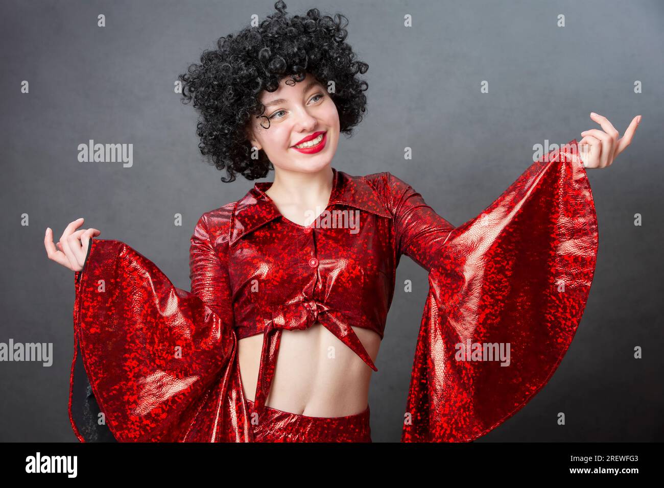 Funny vintage woman in afro wig and disco costume on a gray background. Girl in the style of the seventies. Stock Photo