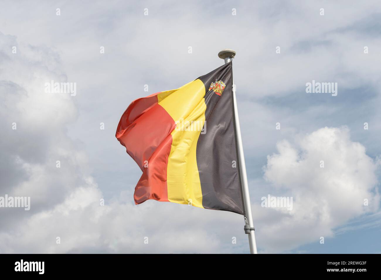 National flag of the Kingdom of Belgium against the background of clouds in the sky. Belgian National Day. Stock Photo