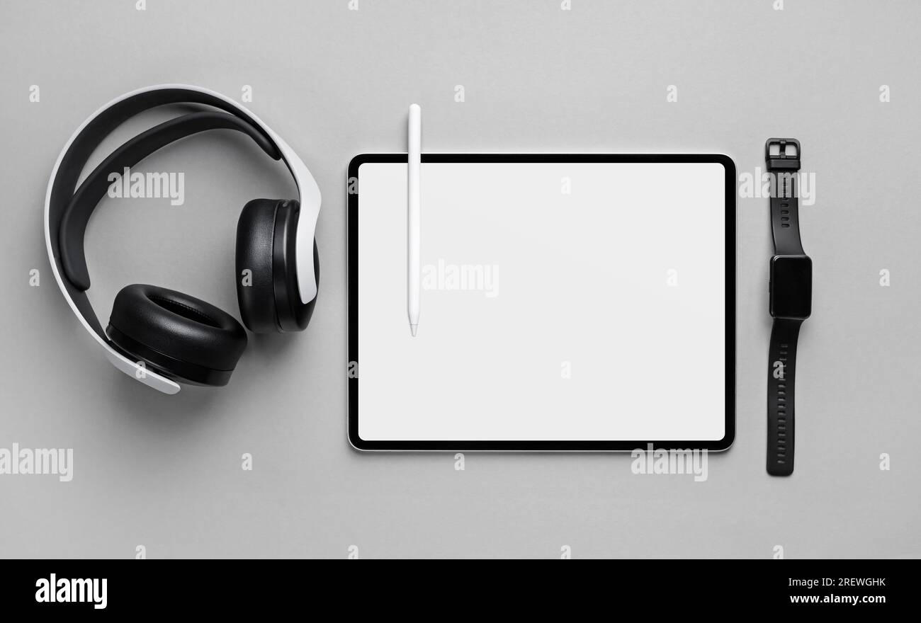 Photo of tablet computer with blank white screen, headphones, fitness bracelet and stylus pen on gray paper background. Top view. Flat lay. Stock Photo