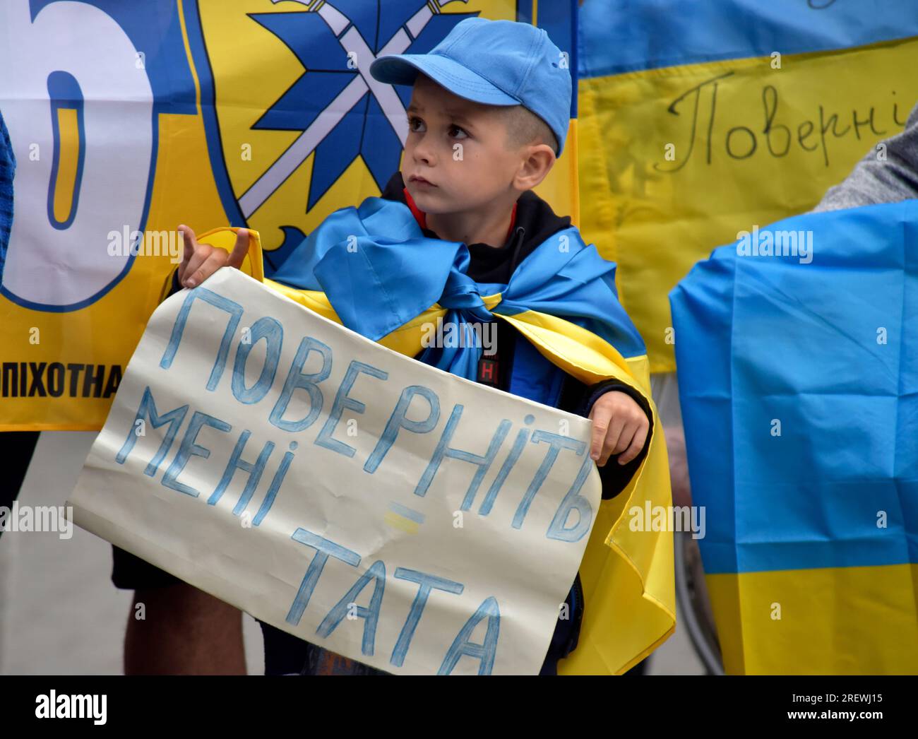 Non Exclusive: VINNYTSIA, UKRAINE - JULY 27, 2023 - A little boy wrapped in a Ukrainian flag holds a placard reading &#x91;Give Me Father Back&#x92; d Stock Photo