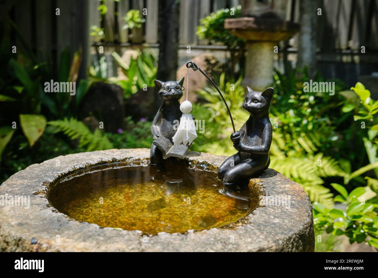 Jun 2023, Kurashiki Bikan Historical Quarter decoration. Two cats sitting on the side of a pond, one is fishing using teru teru bozu talisman as bait Stock Photo