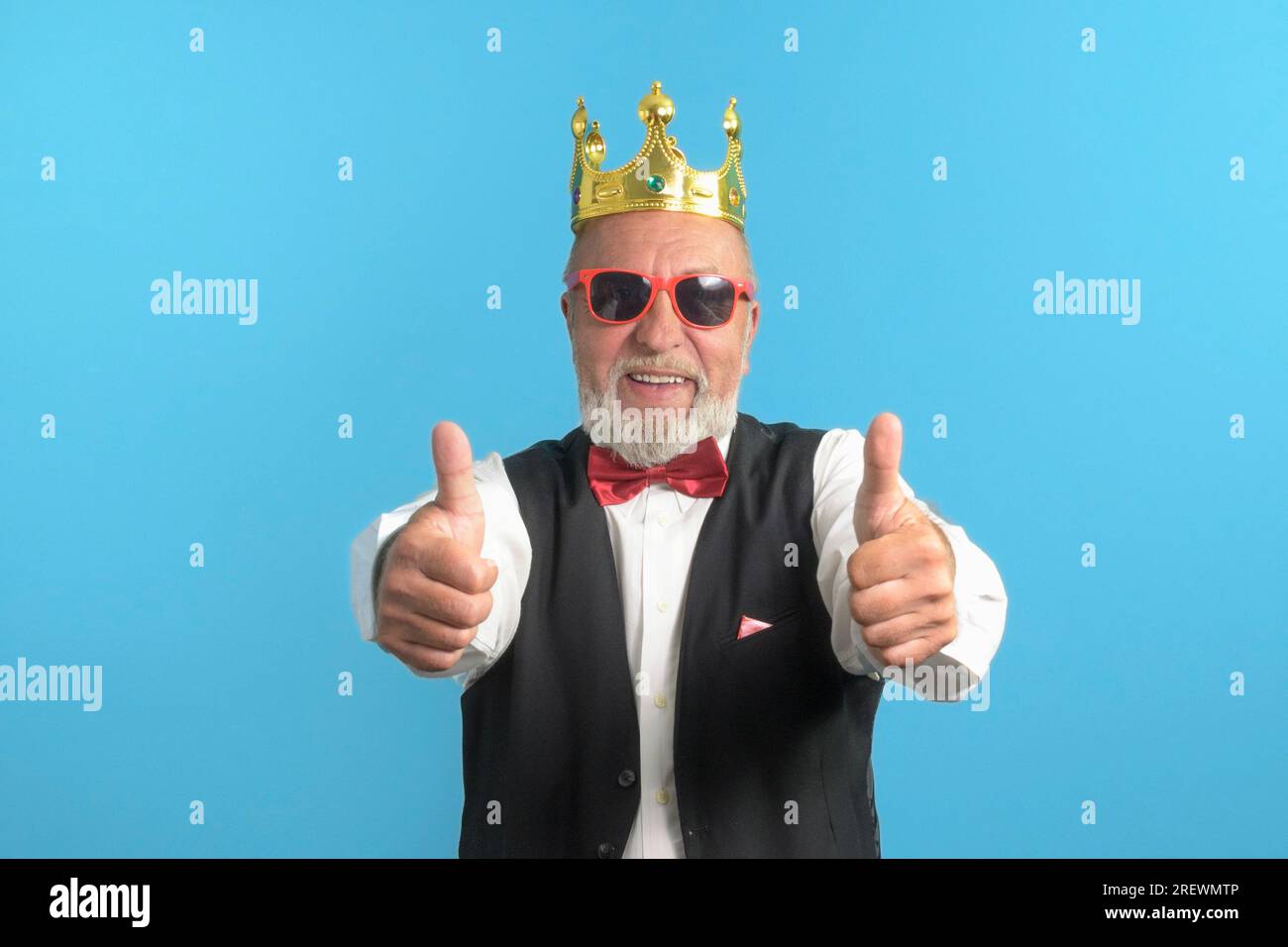 Funny old man in a festive suit on a blue background with a bow tie and a golden crown on his head Stock Photo