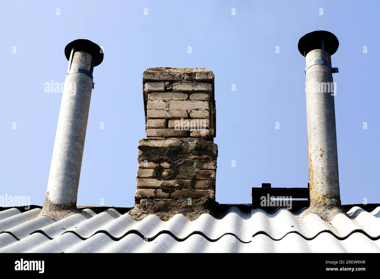 the upper part of the roof with slate and pipes made of bricks and metal pipes for heating the house with firewood and coal, against the blue sky chim Stock Photo