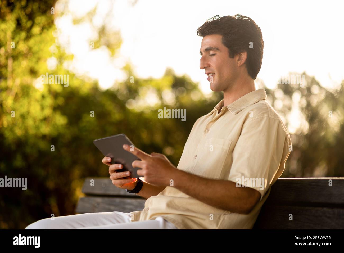 Young man digital nomad sitting on bench, using tablet Stock Photo