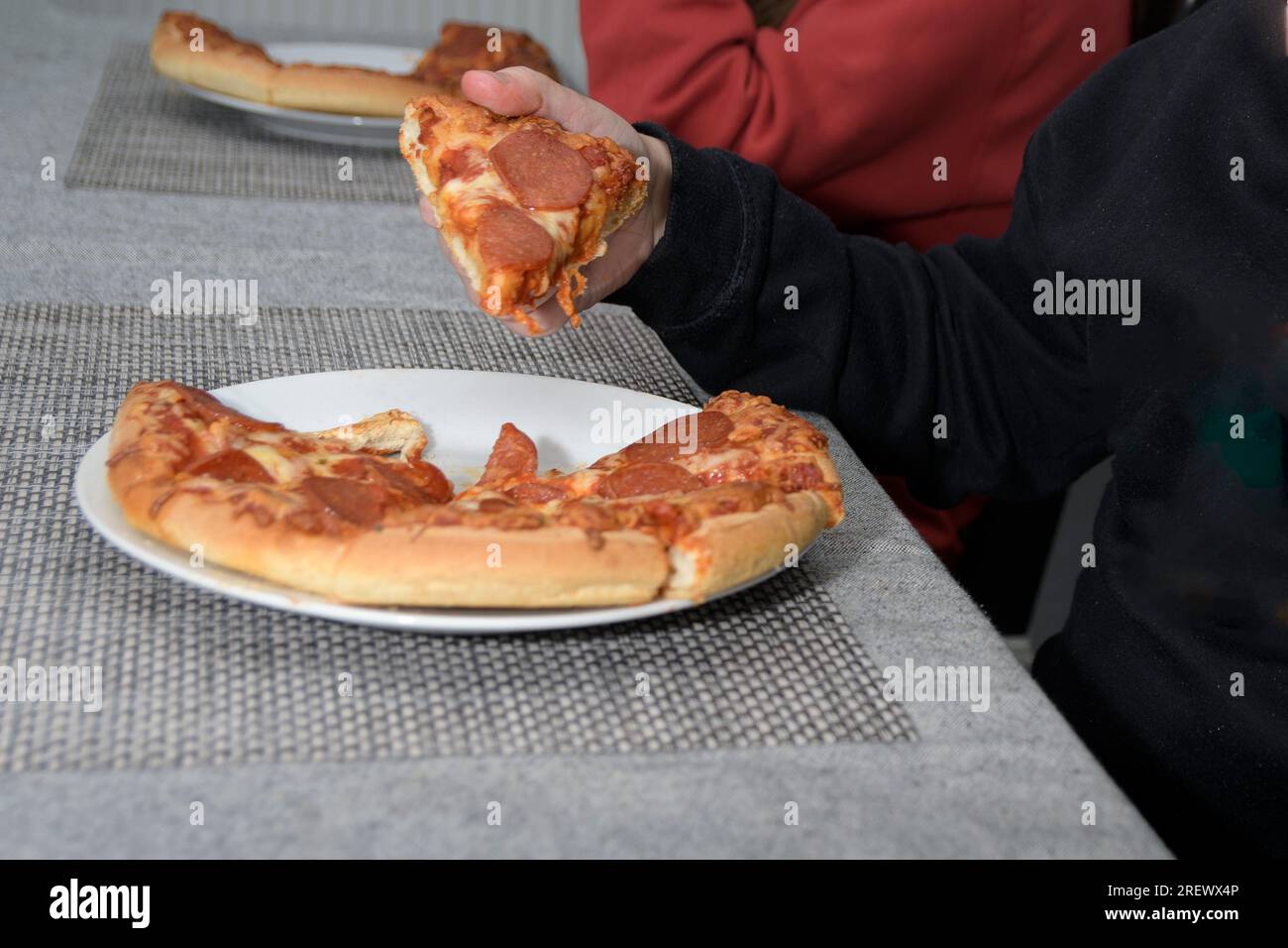 The child takes pizza from a white plate on the table. Close-up hand and piece Stock Photo