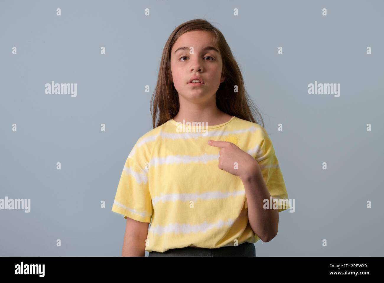 Why me. A teenage girl points her finger at herself. Questioning look. Yellow T-shirt. Gray background Stock Photo