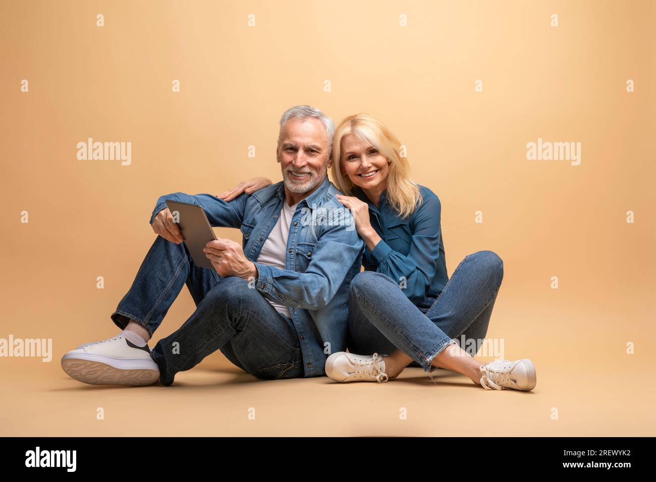 Positive senior spouses using digital tablet, beige background Stock Photo