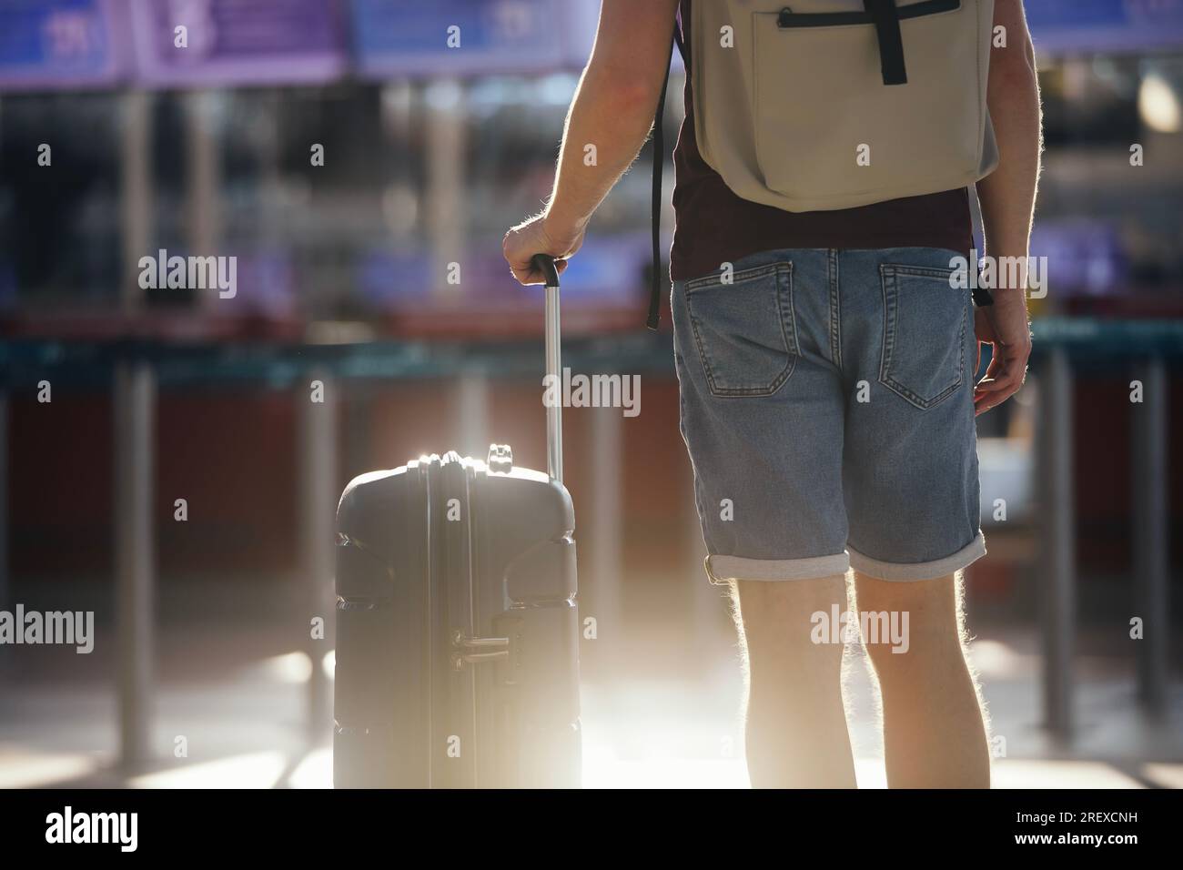 Traveling by airplane. Selective focus on hand of man holding suitcase. Traveler walking with luggage through airport terminal towards check-in. Stock Photo