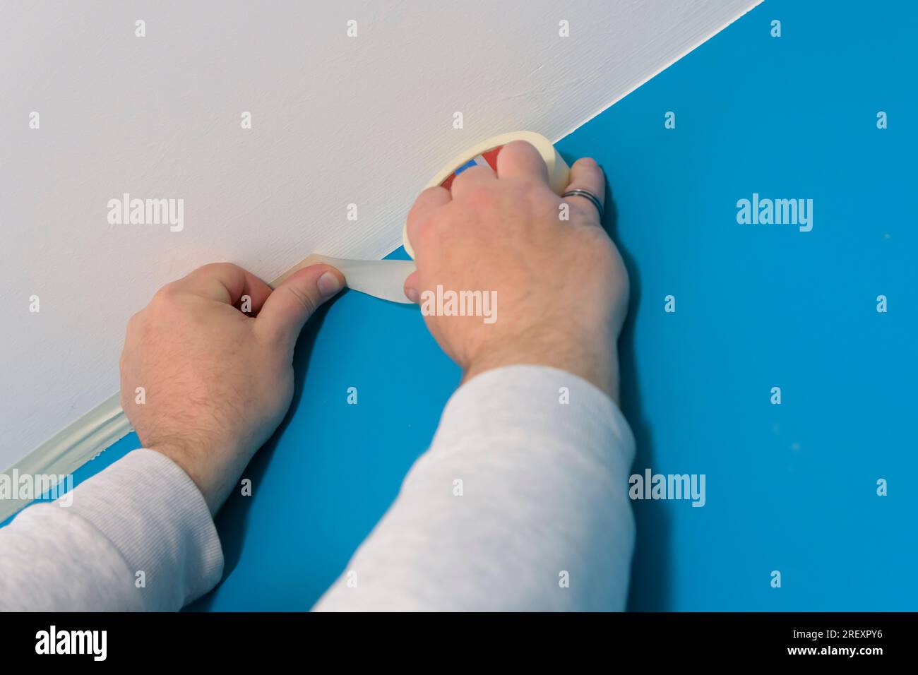 Applying masking tape between white ceiling and colored wall to be painted Stock Photo Alamy